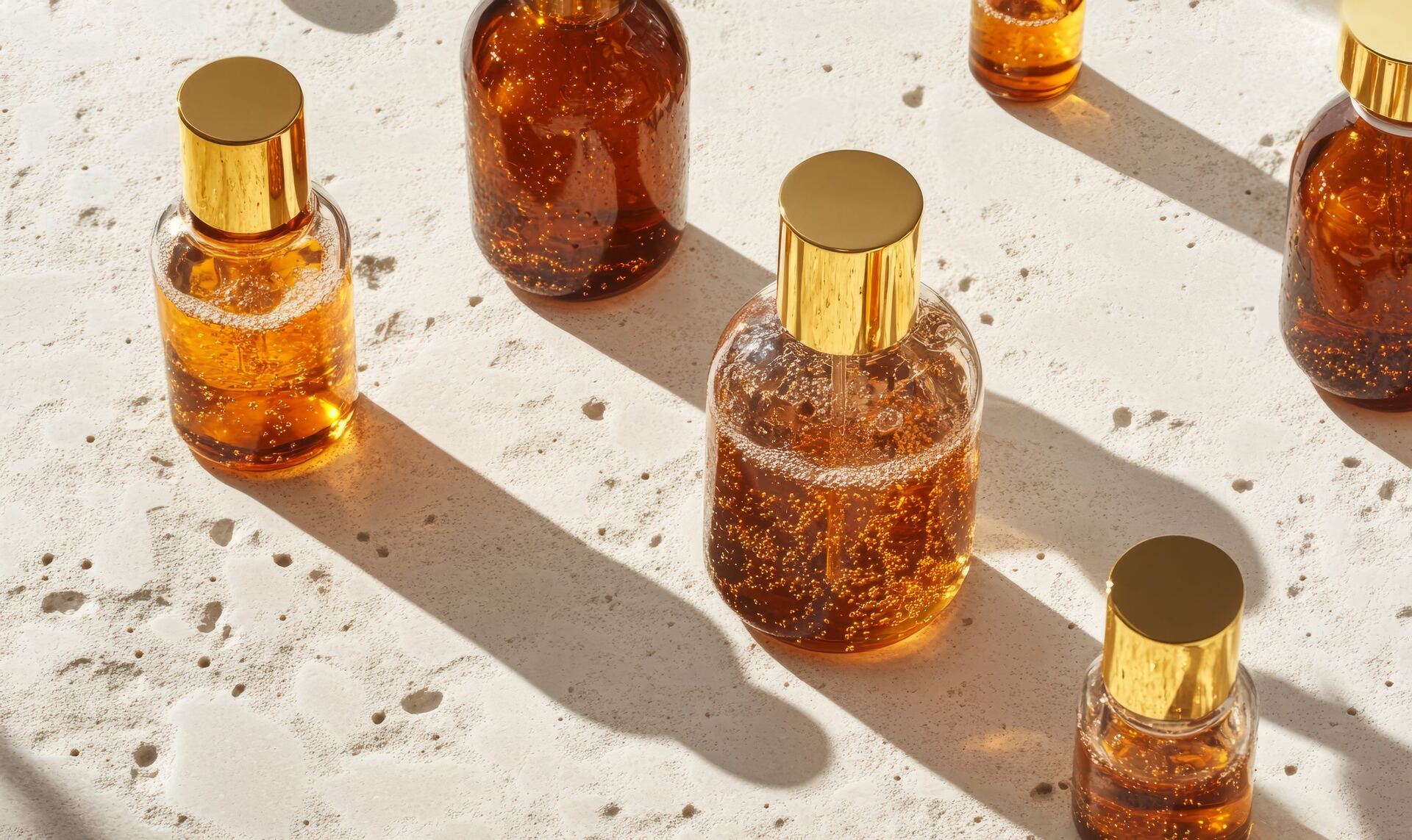 Amber glass bottles with golden caps on travertine in the sun